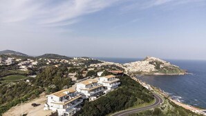 An aerial view of a coastal town with modern buildings, a winding road, and a prominent hill with a fort-like structure. - Castelsardo Apartment - Between Blue and Heavenly A beautiful view of the sea (Castelsardo)