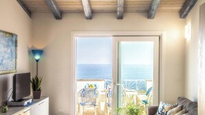 A room with a television, a potted plant, and a view of the sea through a glass door. - Castelsardo Apartment - Between Blue and Heavenly A beautiful view of the sea (Castelsardo)
