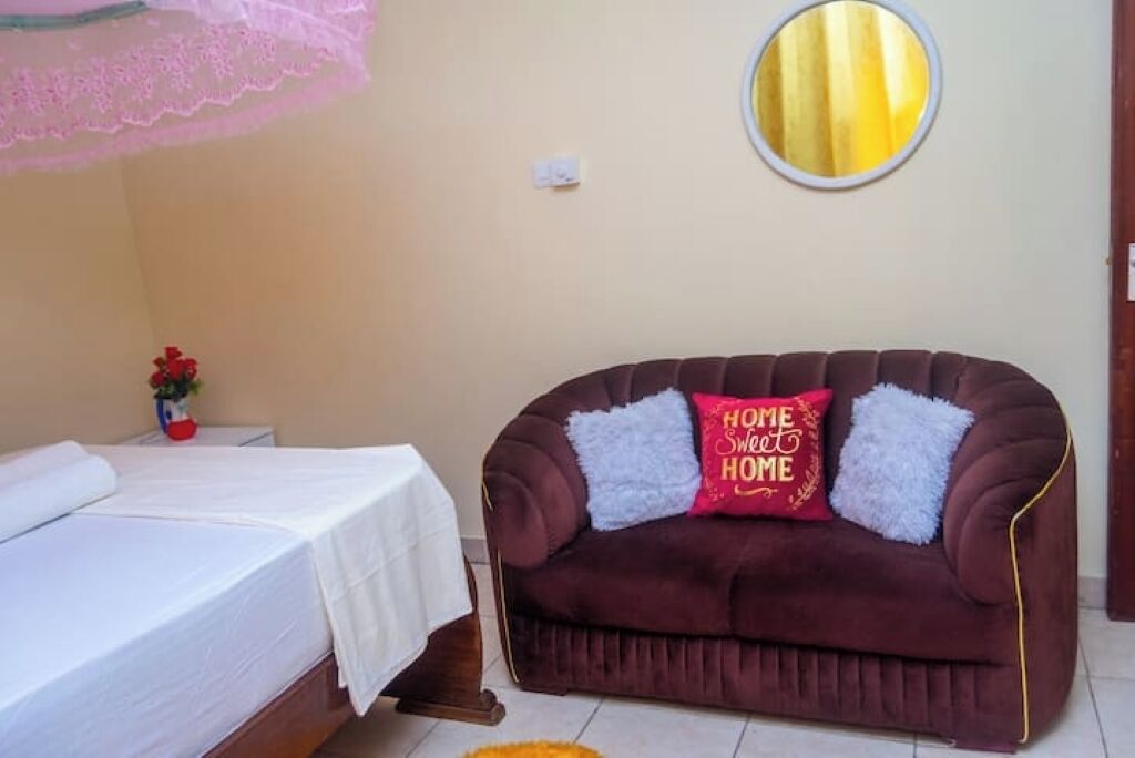 Une chambre à coucher avec un lit, un canapé marron avec des coussins, une petite table avec un vase et un miroir rond accroché au mur.