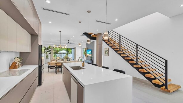 Una cocina moderna con una isla central, un comedor y una escalera.