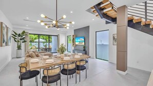 Un comedor moderno con una mesa de madera, sillas negras de mimbre y una lámpara de araña contemporánea.