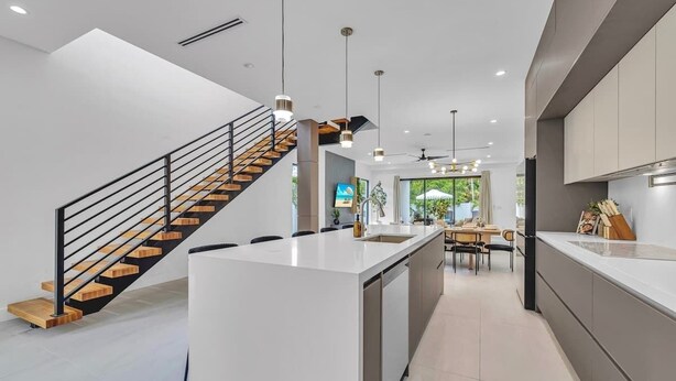 Une cuisine moderne dotée d ’un îlot central, d’un escalier avec des marches en bois, d’un éclairage suspendu et d’un coin repas offrant une vue agréable.