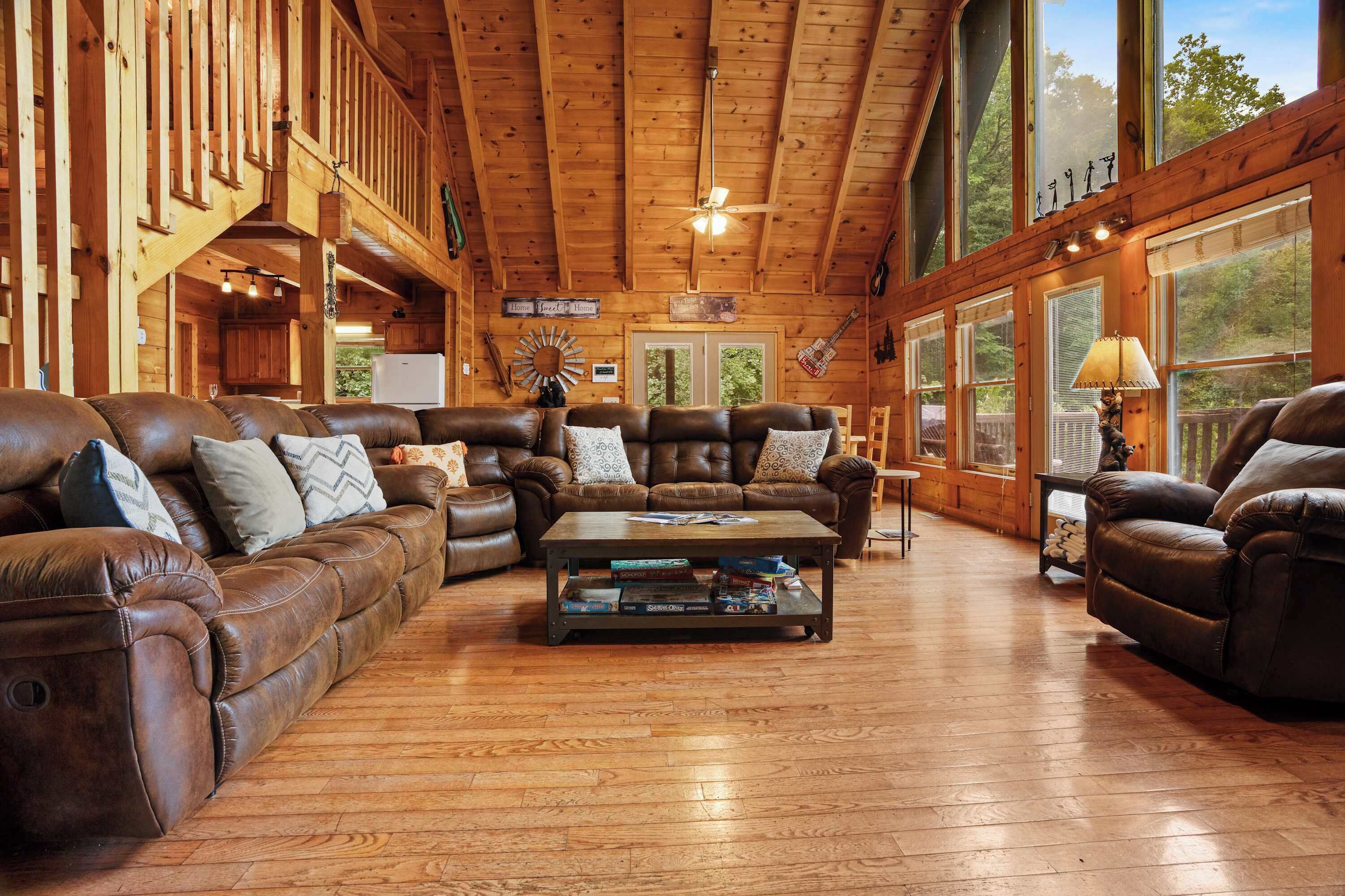 A spacious living room with leather sofas, a coffee table, and large windows offering a view of the outdoors.