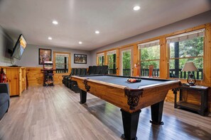 Une table de billard dans une pièce aux murs en bois et aux grandes fenêtres.