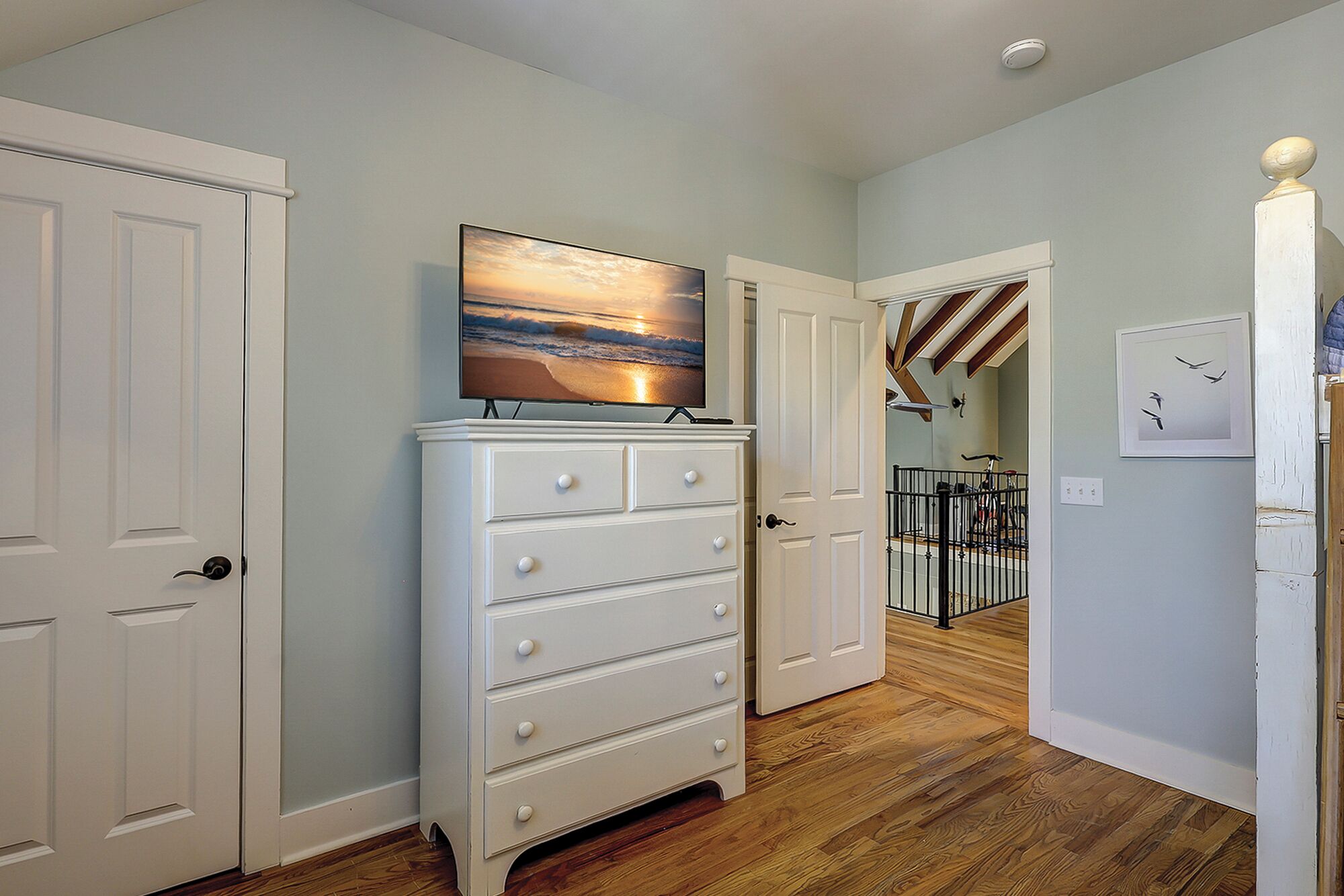 A hallway with a white dresser, a painting of a sunset, and a staircase leading to another room.
