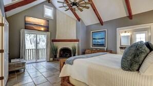 A bedroom with a large bed, a fireplace, a ceiling fan, and a view of the outdoors. - 50 Dune Lane – NFB Oceanside Retreat- Private Pool, Steps from the Beach (Hilton Head Island)