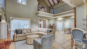 A spacious living area with a high ceiling, a multi-level balcony, and a dining area with wicker chairs. - 50 Dune Lane – NFB Oceanside Retreat- Private Pool, Steps from the Beach (Hilton Head Island)