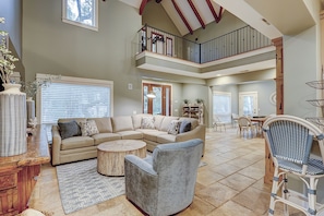 A spacious living area with a high ceiling, a multi-level balcony, and a dining area with wicker chairs. - 50 Dune Lane – NFB Oceanside Retreat- Private Pool, Steps from the Beach (Hilton Head Island)