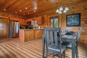 A wooden cabin interior with a kitchen area, a dining table with chairs, and a chandelier. - Handicap Friendly Cabin Retreat・Pool Table・Grill (Pigeon Forge)