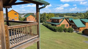 A wooden cabin with a green roof, surrounded by a well-maintained lawn and other cabins in a mountainous area. - Handicap Friendly Cabin Retreat・Pool Table・Grill (Pigeon Forge)