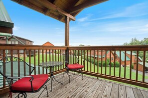 A wooden deck with two chairs and a table, overlooking a green lawn and a wooden cabin. - Handicap Friendly Cabin Retreat・Pool Table・Grill (Pigeon Forge)