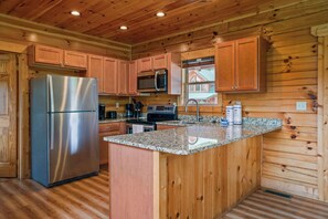 A kitchen with wooden cabinets, a stainless steel refrigerator, a microwave, and granite countertops. - Handicap Friendly Cabin Retreat・Pool Table・Grill (Pigeon Forge)