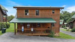 A two-story log cabin with a green metal roof, a porch with a railing, and signs indicating reserved parking and accessible entrance. - Handicap Friendly Cabin Retreat・Pool Table・Grill (Pigeon Forge)