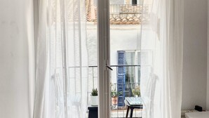 Una habitación con puerta de vidrio corredera que da a un balcón. El piso es de madera y las paredes son blancas.