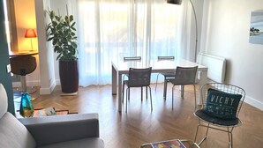 Ett modernt vardagsrum med en soffa, ett matbord med stolar, en krukväxt och en lampa.