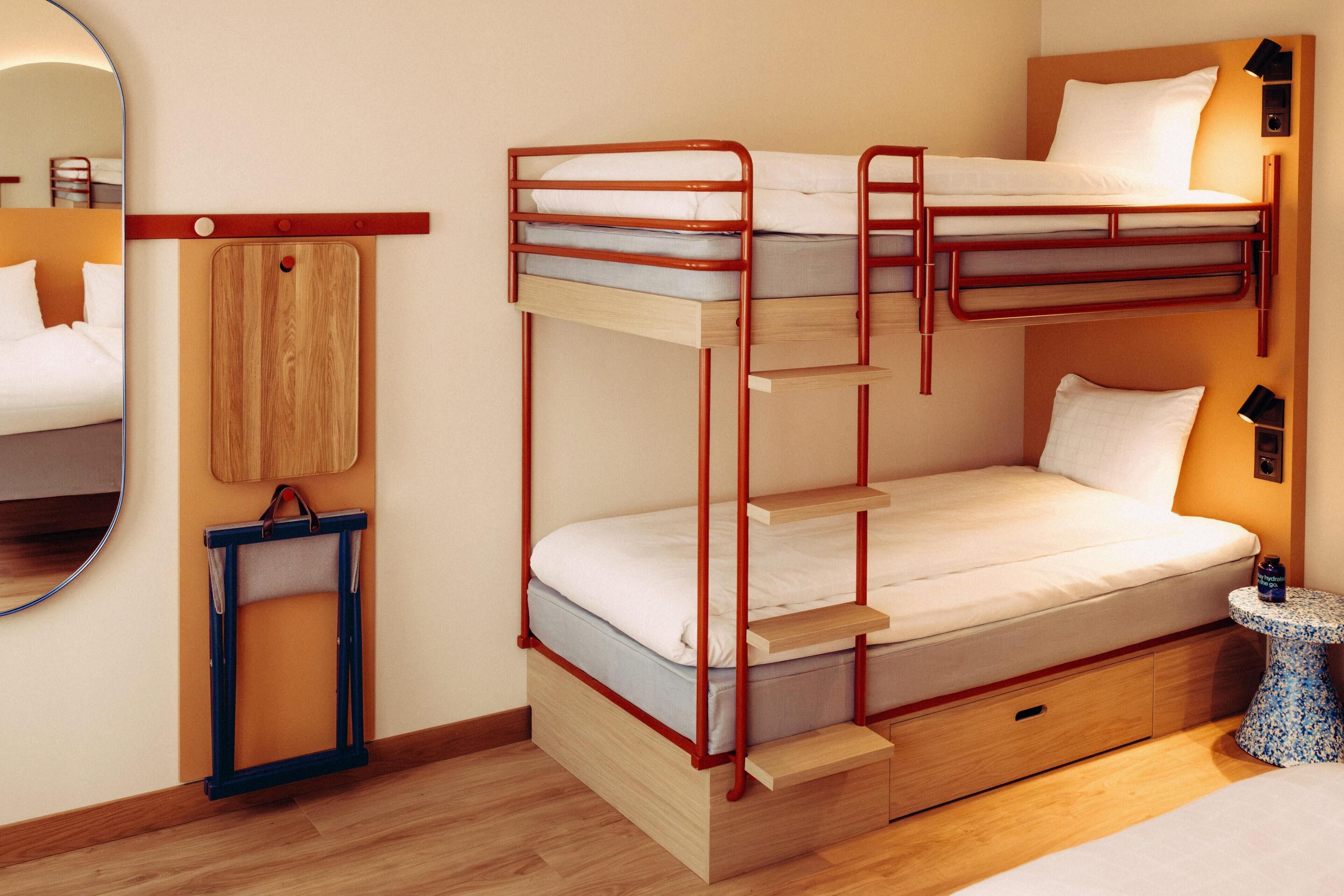 Un lit superposé avec une structure en bois, une petite table de chevet, un miroir et un plancher en bois.