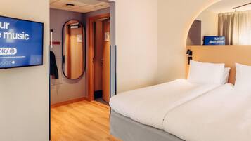 Una habitación de hotel con una cama, televisor, espejo y puerta.