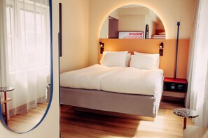 A neatly made bed in a hotel room with a wooden floor, a small table, and a nightstand with a lamp. - Scandic Go, Lilla Bommen 5 (Gothenburg)