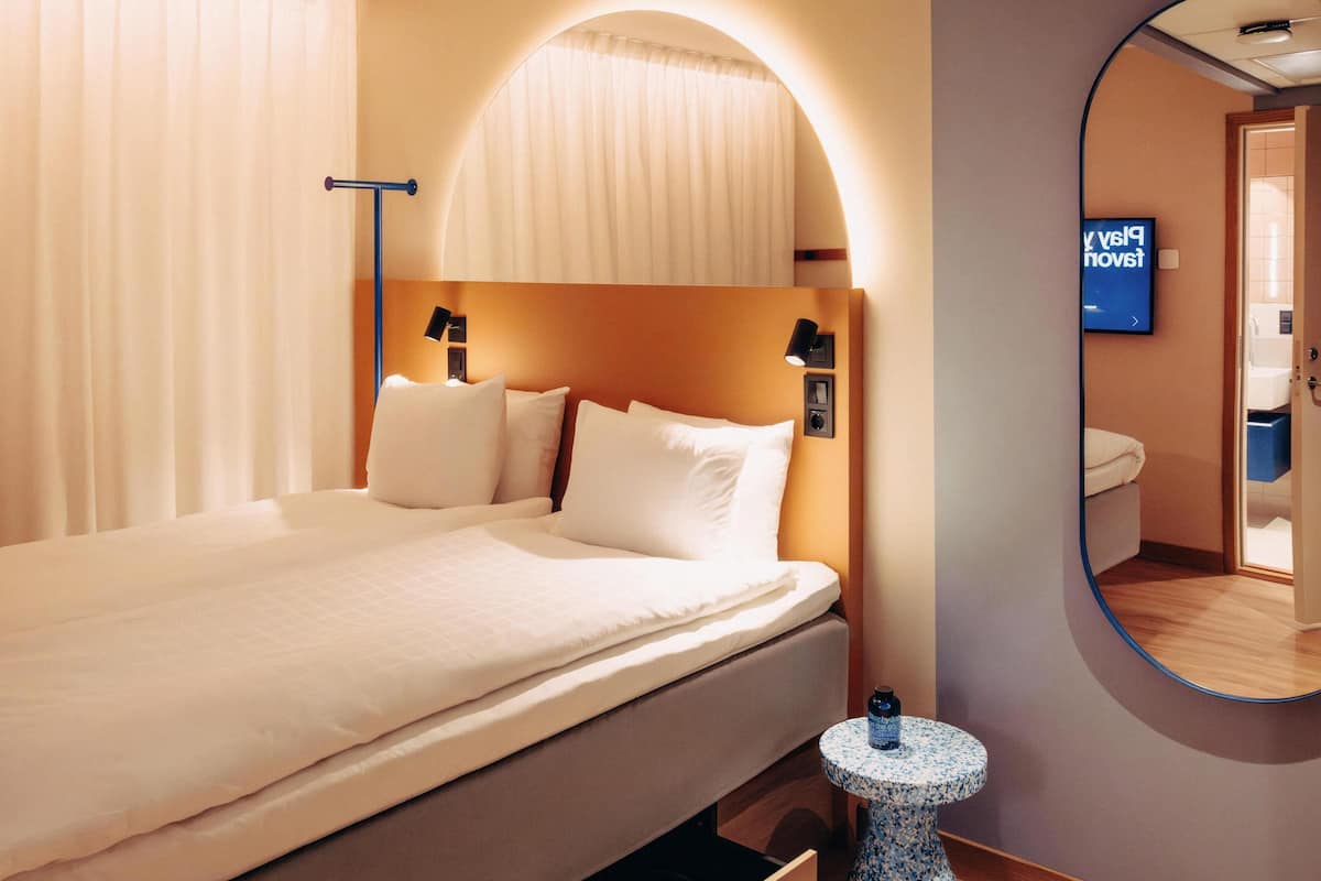 Una habitación de hotel con cama, un espejo redondo, una mesita de noche y una pantalla de televisión.