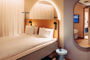A hotel room with a bed, a round mirror, a bedside table, and a TV screen. - Scandic Go, Lilla Bommen 5 (Gothenburg)