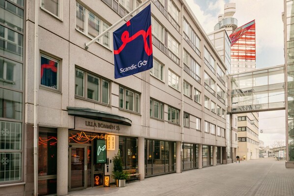 A modern building with a Scandic Go sign, a Lilla Bommenen store, and a glass facade. - Scandic Go, Lilla Bommen 5 (Gothenburg)