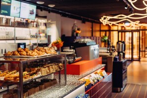 Mostrador de pastelería con bollos, sándwiches, una máquina de café y un menú a la vista.