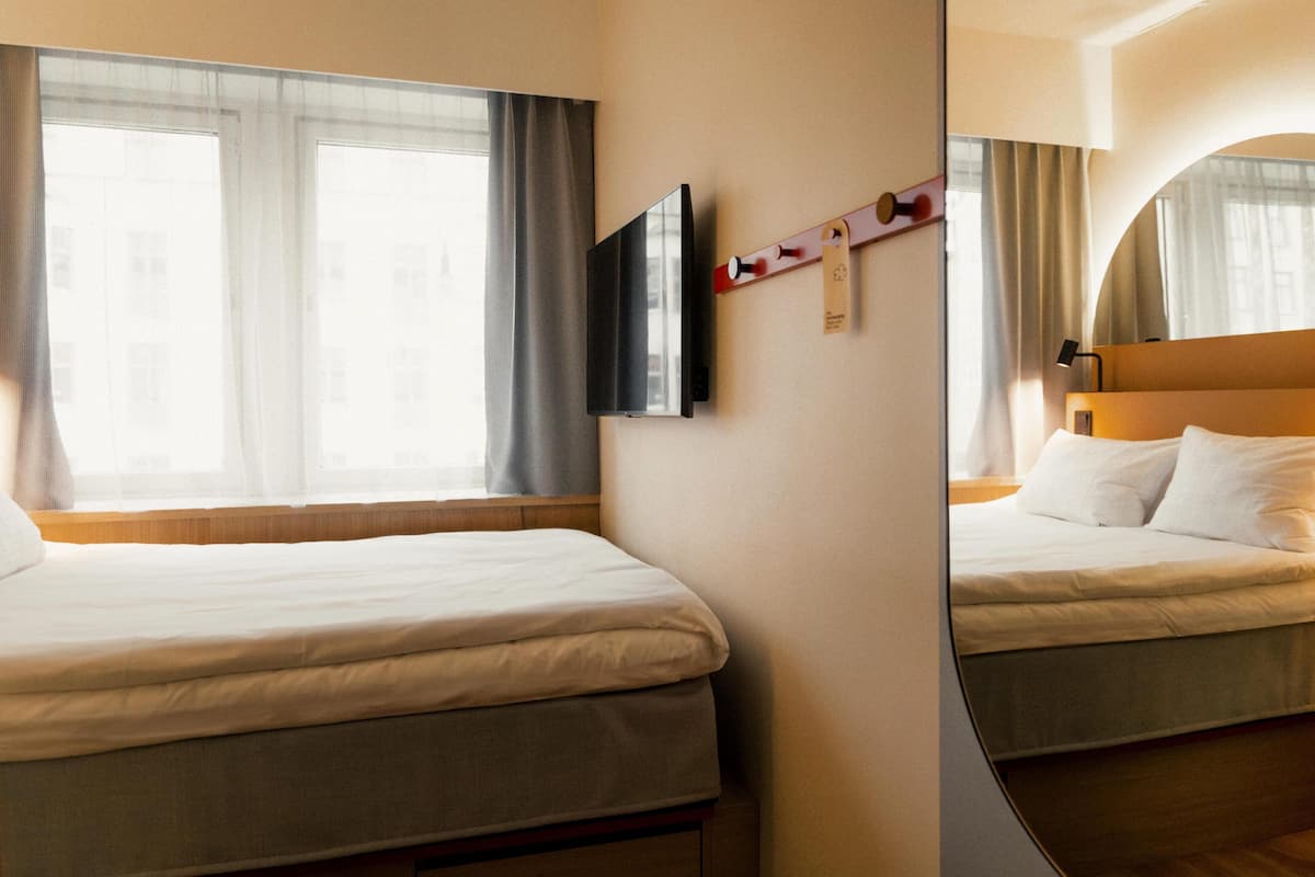 Habitación de hotel con dos camas, un televisor de pantalla plana montado en la pared y una ventana con cortinas.