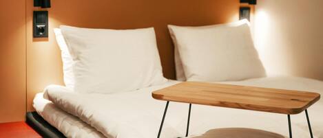 A neatly made bed with white linens, a wooden bedside table, and black wall-mounted lights.