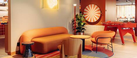 A modern lounge area with a sofa, chairs, a foosball table, and a dartboard.