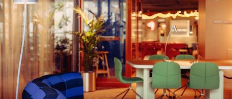 Un café moderno con un sofá azul, sillas verdes, una mesa de madera con dos tazas y una planta grande en maceta.