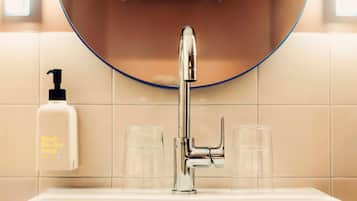 Une salle de bain avec un robinet chromé, un distributeur de savon et deux verres transparents posés sur le lavabo.