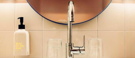 Un baño con un grifo cromado, un dispensador de jabón y dos vasos de cristal en el lavabo.