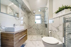 A modern bathroom with a marble floor, a wooden vanity, a white toilet, a glass shower enclosure, and a small window. - 1Bed · Cardiff Centre · Sleeps 2 (Cardiff)