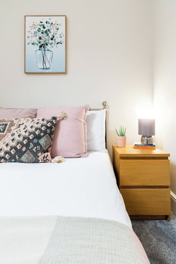 A neatly made bed with a patterned pillow, a bedside table with a lamp and a small plant, and a framed artwork above the bed. - 1Bed · Cardiff Centre · Sleeps 2 (Cardiff)