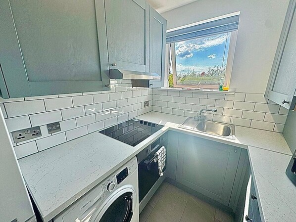 Une cuisine de taille réduite avec des meubles gris, un four encastré, un évier et une fenêtre donnant sur l’extérieur.