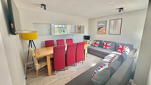 Un espace de vie compact comprenant un coin repas, un canapé orné de drapeaux britanniques et des œuvres d’art accrochées aux murs.