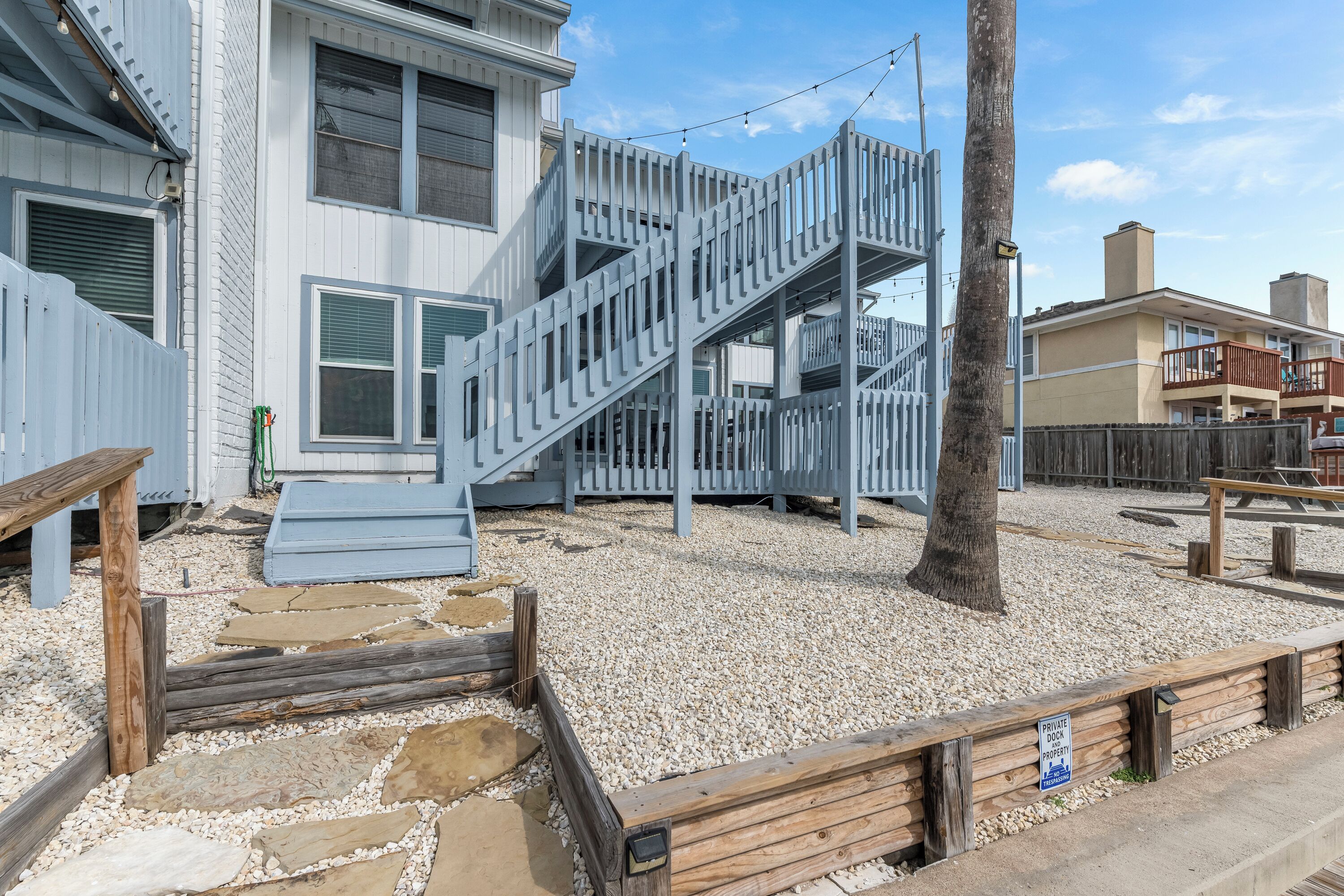 A residential building with a two-story staircase, a wooden deck, and a gravel pathway.