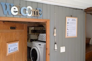 A laundry area with a 'Welcome' sign, a private room door, a washing machine, and a sign with laundry instructions.