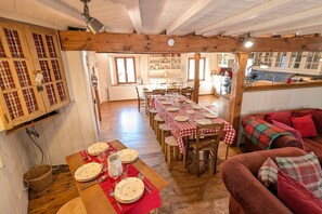 Un comedor con una larga mesa de madera dispuesta para una comida, un sofá rojo acogedor y una cocina al fondo.