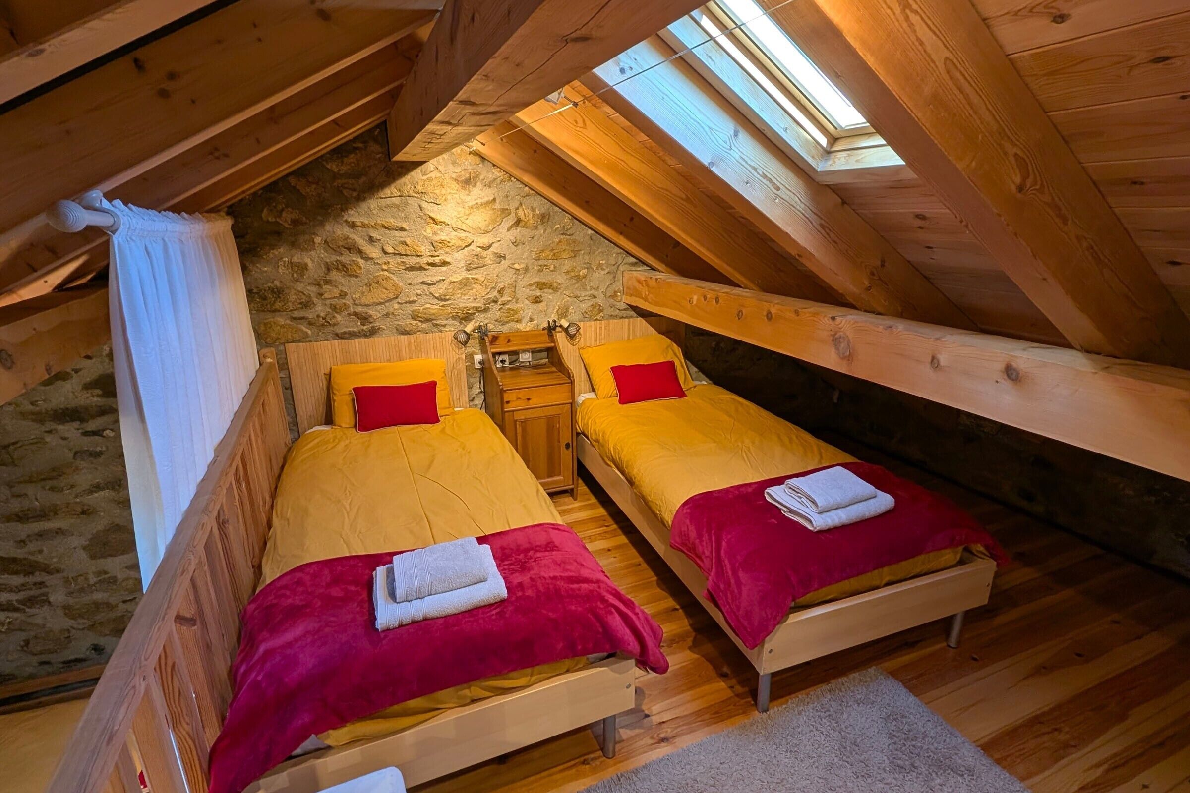 Une chambre mansardée chaleureuse, avec deux lits, un mur en pierre et une lucarne.