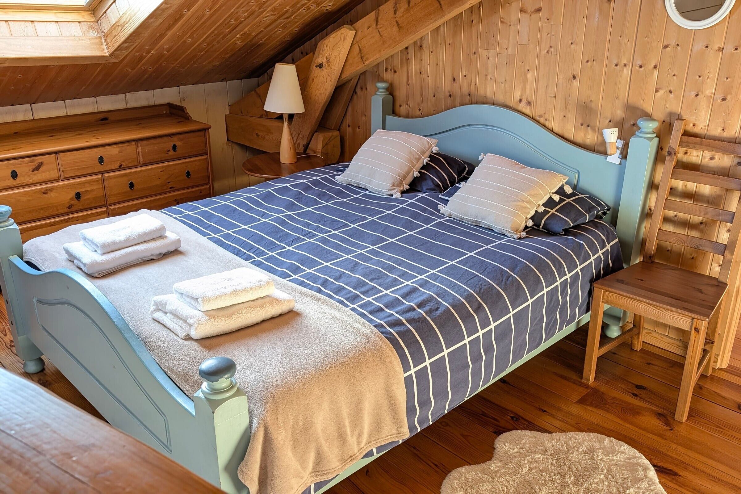 Une chambre à coucher avec un lit, une commode en bois, une table de chevet, une lampe et une échelle.