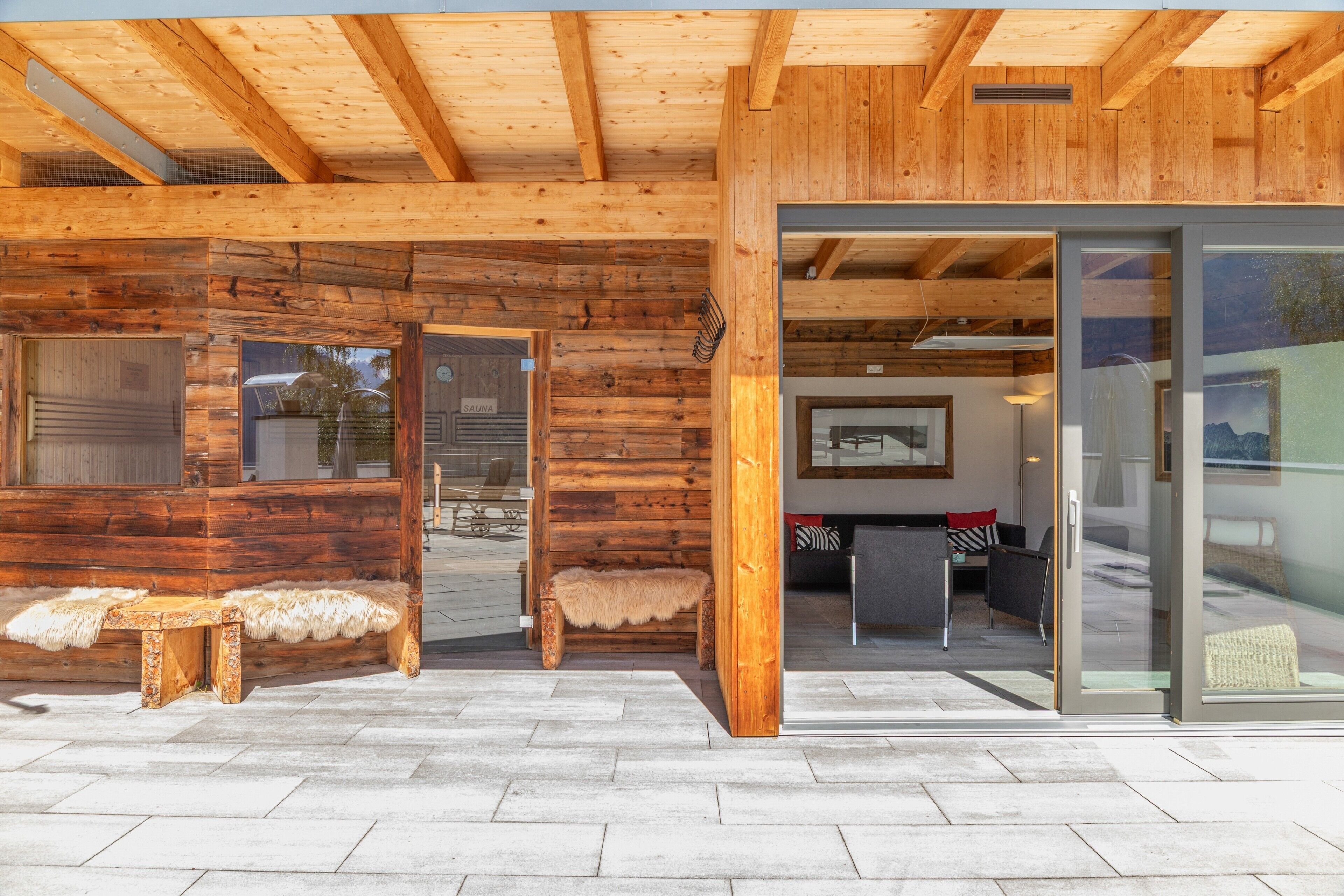Eine Holzhütte mit Sauna, Glastür und einer Sitzecke mit einem Fellbank.