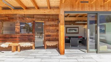Eine Holzhütte mit Sauna, Glastür und einer Sitzecke mit einem Fellbank.
