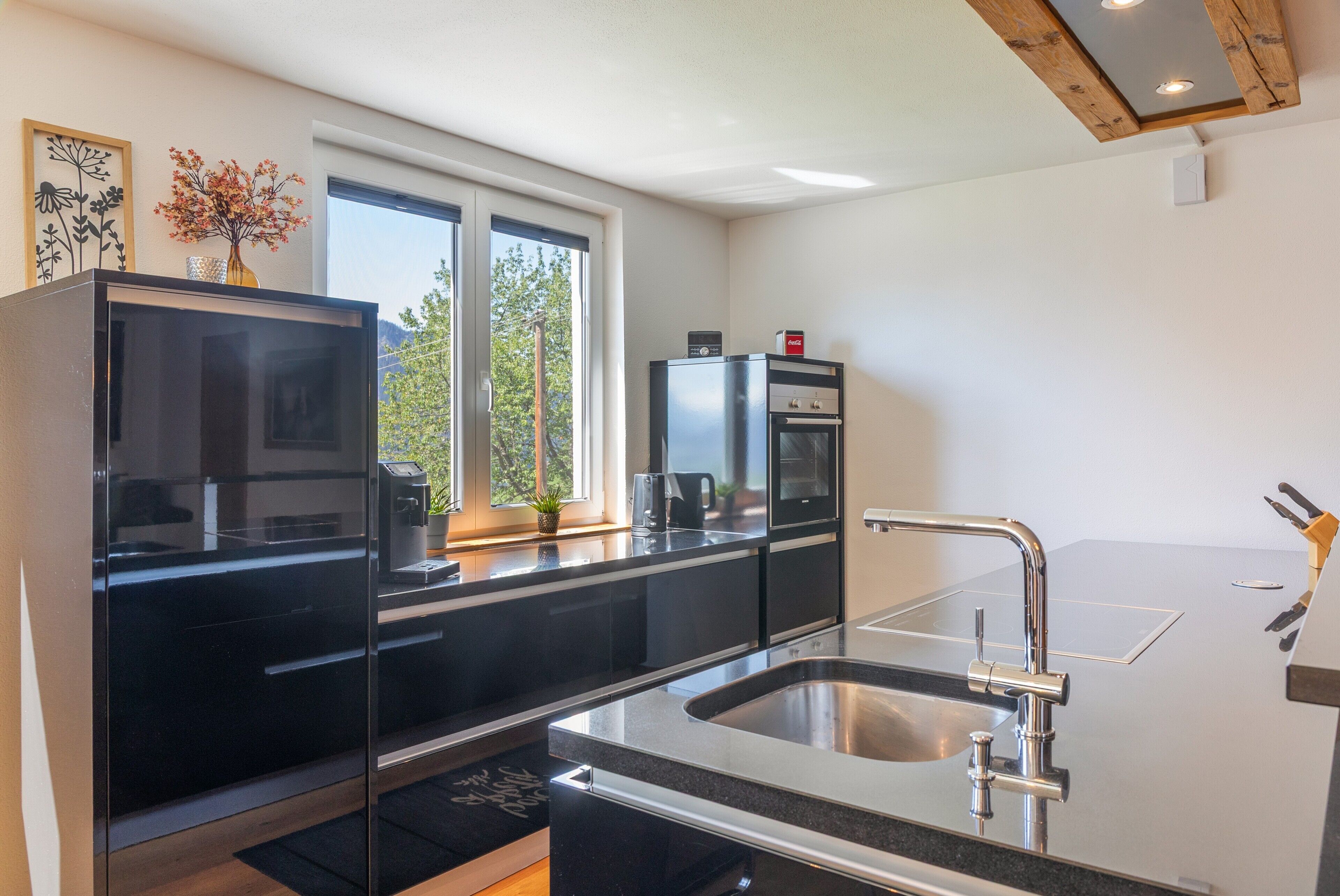 A modern kitchen with a black refrigerator, a coffee machine, and a sink with a stainless steel faucet.