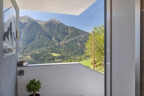 A balcony with a mountain view, a small potted plant, and a sign with the word 'ALPEN'.