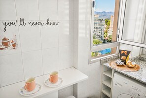 A modern kitchen with a window view, a countertop with a gift basket, and a wall with a partial text. - Apartment Sea View 10 Gandía (Grau i Platja)