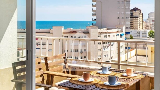 Uma varanda com mesa e cadeiras de madeira, com vista para a cidade e o mar.