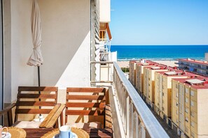 A balcony with wooden furniture, a white curtain, and a view of the beach and ocean. - Apartment Sea View 10 Gandía (Grau i Platja)