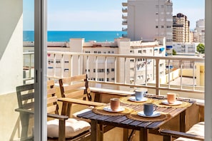 A balcony with a wooden table, chairs, and a view of the sea and buildings. - Apartment with Ocean View 10, Gandía (Grau i Platja)