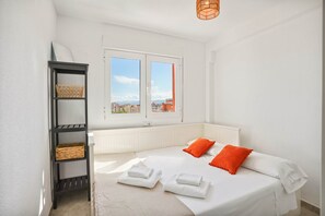 A bedroom with a bed, two pillows, a shelf with baskets, a window with a view, and a radiator. - Apartment Sea View 10 Gandía (Grau i Platja)